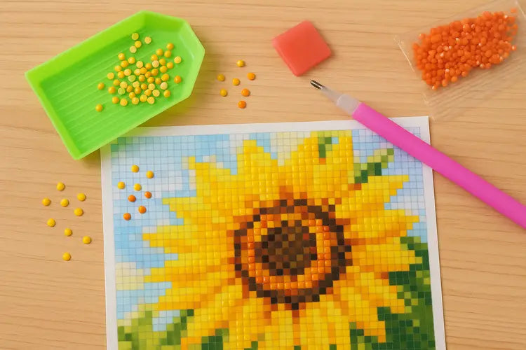Close-up van diamond painting met zonnebloem, ronde steentjes, wax pen en sorteerbakje op tafel