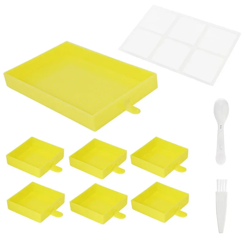 Set met zes vierkante diamond painting bakjes in het geel, inclusief transparant deksel, scheplepel en wit schoonmaakborsteltje op witte achtergrond